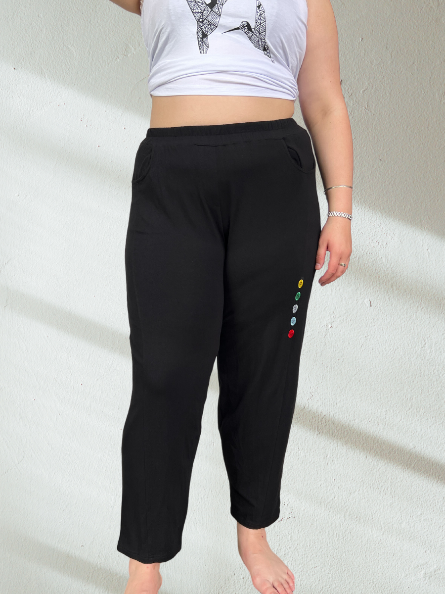 A plus-size woman wearing black relaxed-fit pants with a comfortable elastic waistband and stylish button details on the side. The pants have a tapered-leg design, functional side pockets, and a soft, stretchable fabric that drapes beautifully over curves.